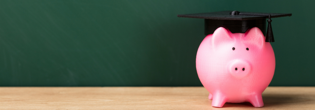 A pink piggy bank wears a graduation cap in front of a green chalkboard.