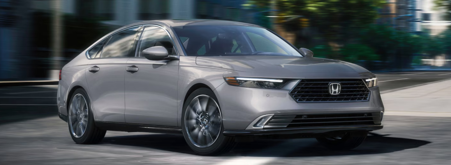 A silver Honda Accord sedan drives on a paved road with blurred background, indicating motion.