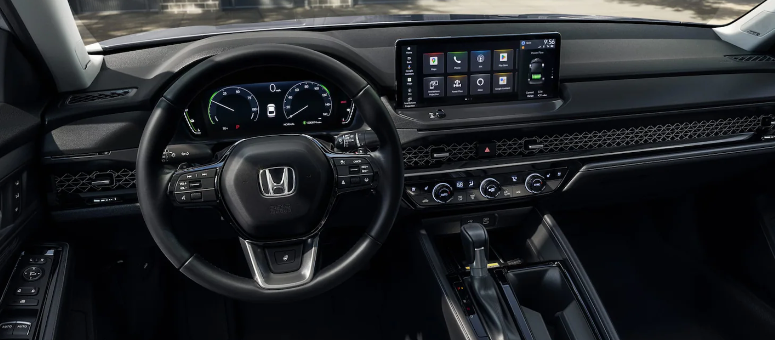 A car's dark interior shows a steering wheel on the left, a digital instrument cluster, and a central touchscreen displaying app icons.