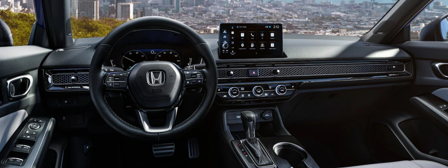 The interior of a car shows a dark dashboard with a steering wheel, a digital instrument cluster, and a central touchscreen displaying app icons, all against a cityscape background seen through the windshield.