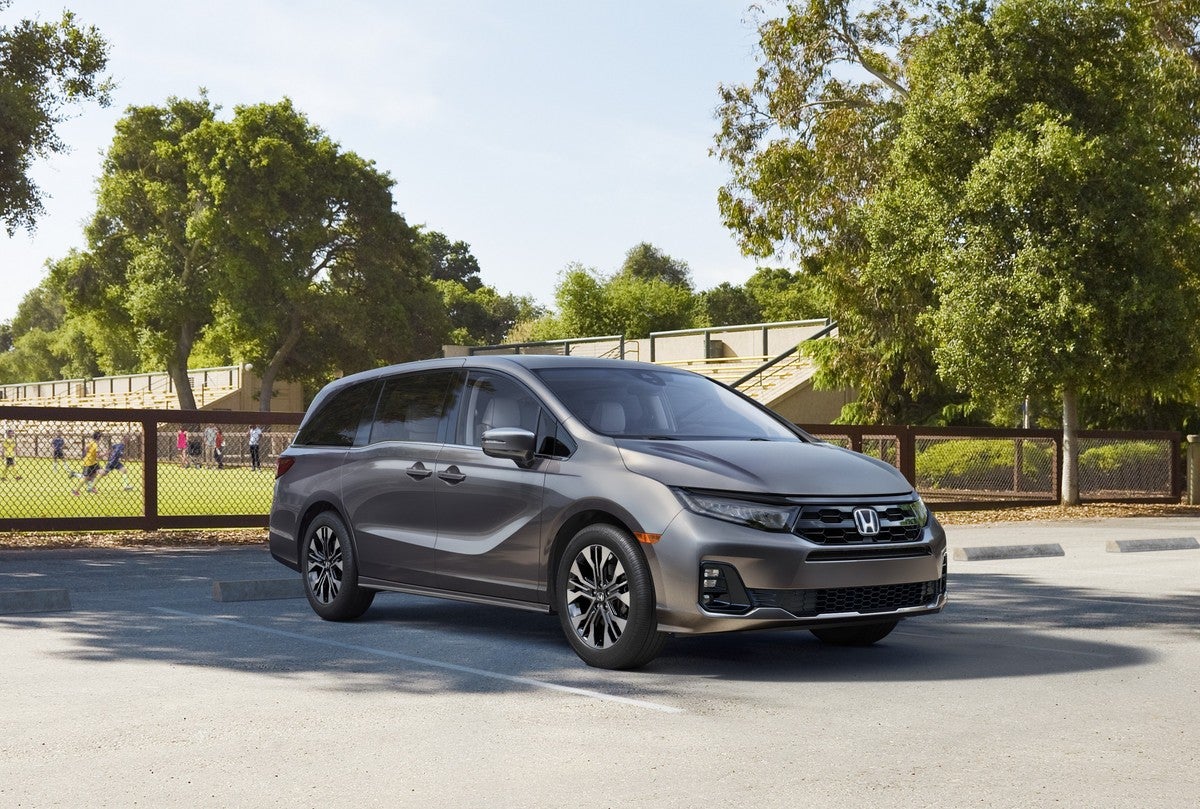 A grey new Honda Odyssey in Phoenix is parked facing the viewer to the right in a small parking lot in front of a soccer field.