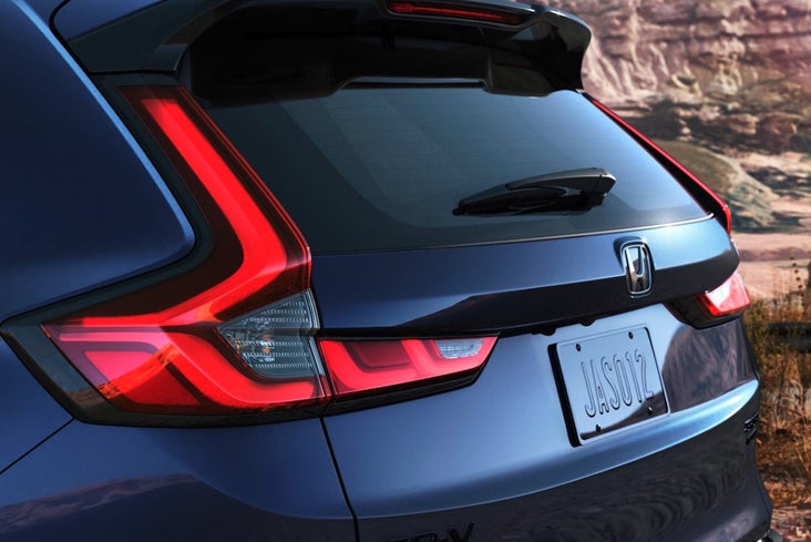 A close-up view of the rear hatch, taillight, and spoiler of a dark blue Honda CR-V parked in a rocky landscape."