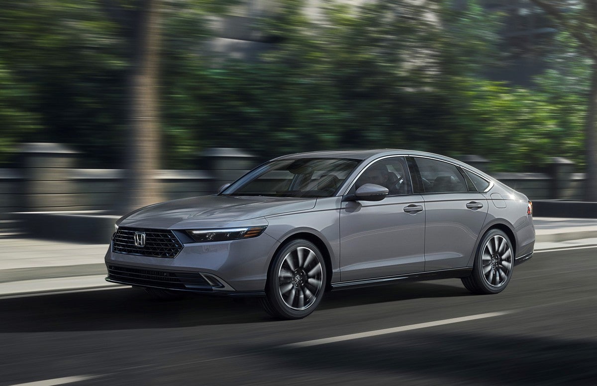 A grey new Honda Accord in Phoenix drives towards the viewer to the left on a city street in front of a park.