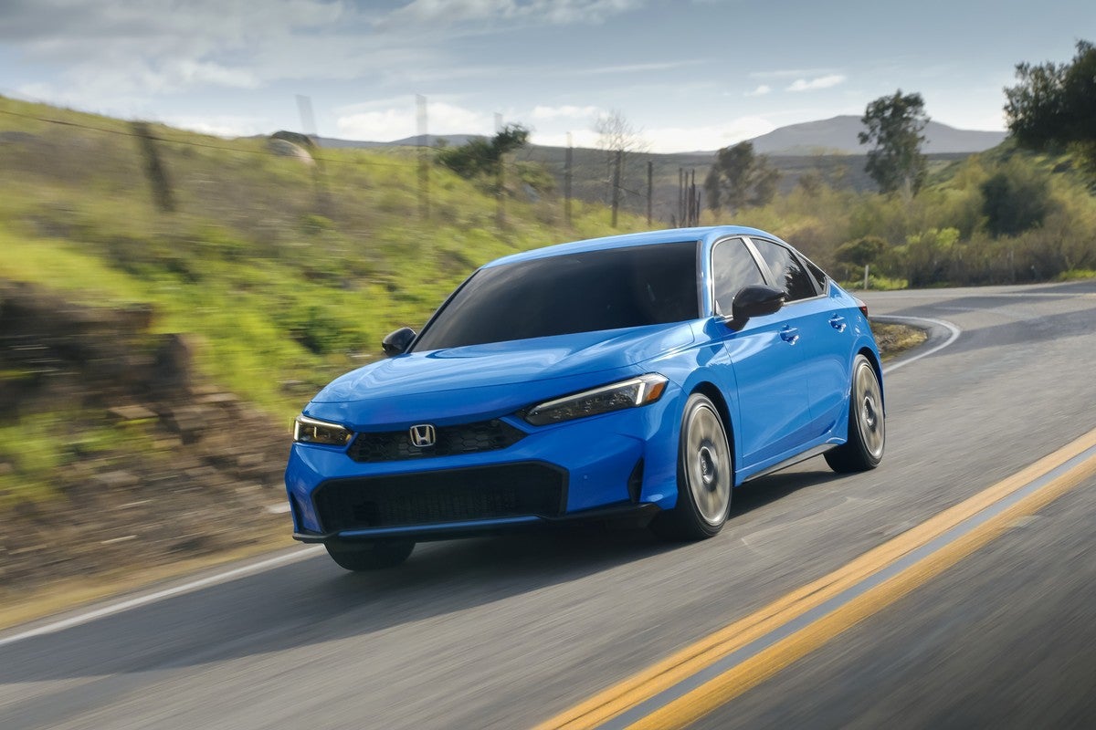 A blue 2026 Honda Civic Hatchback in Phoenix drives towards the viewer to the left on a curvy country road through farmland.