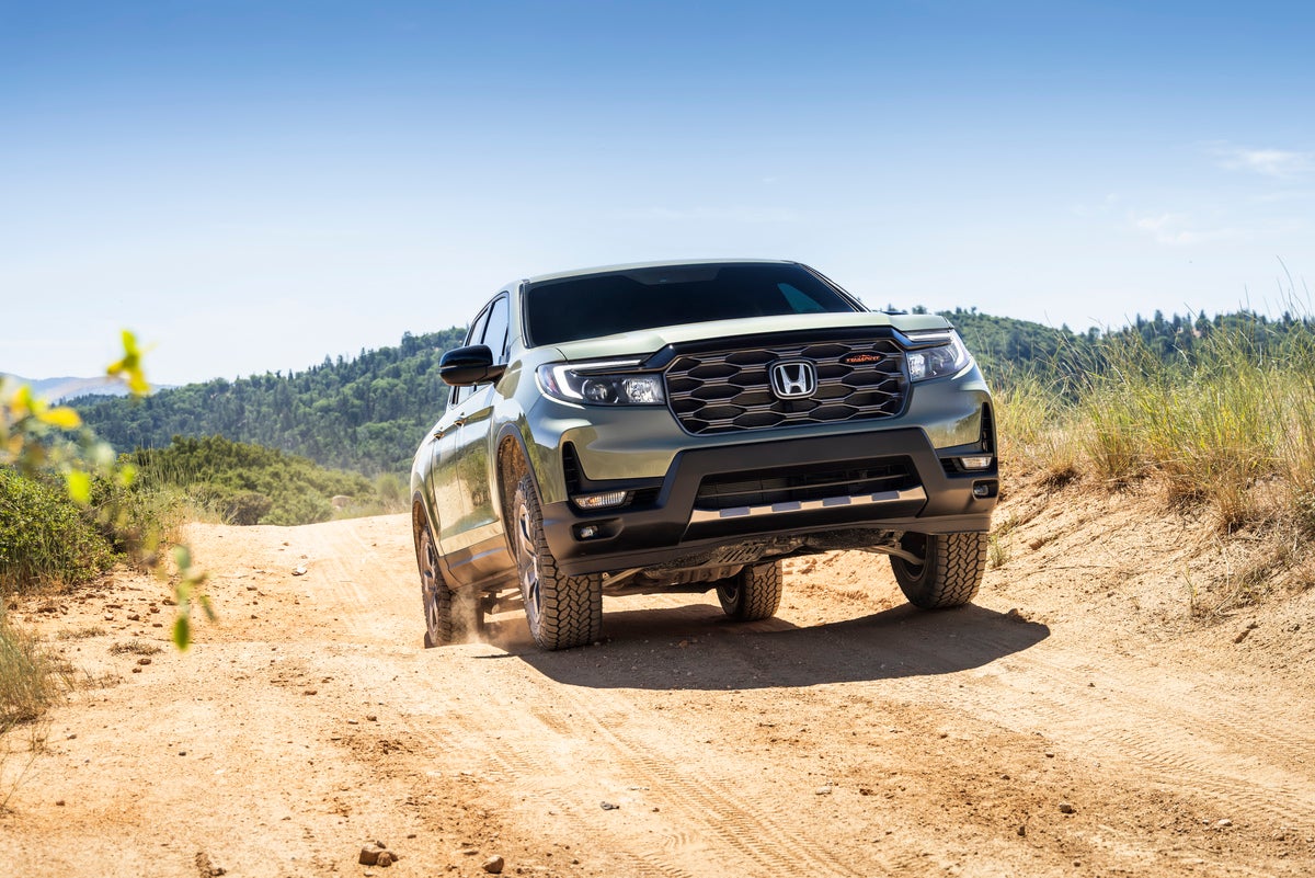 A Green American Made Hona Ridgeline in Phoenix drives towards the viewer to the right up a rocky dirt trail in the wilderness.