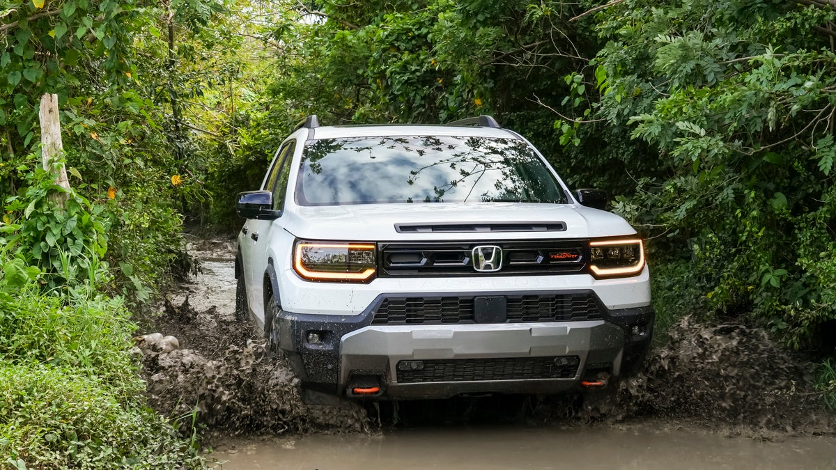 A white used Honda Passport in Phoenix drives towards the viewer through a narrow stream, kicking up mud behind it.