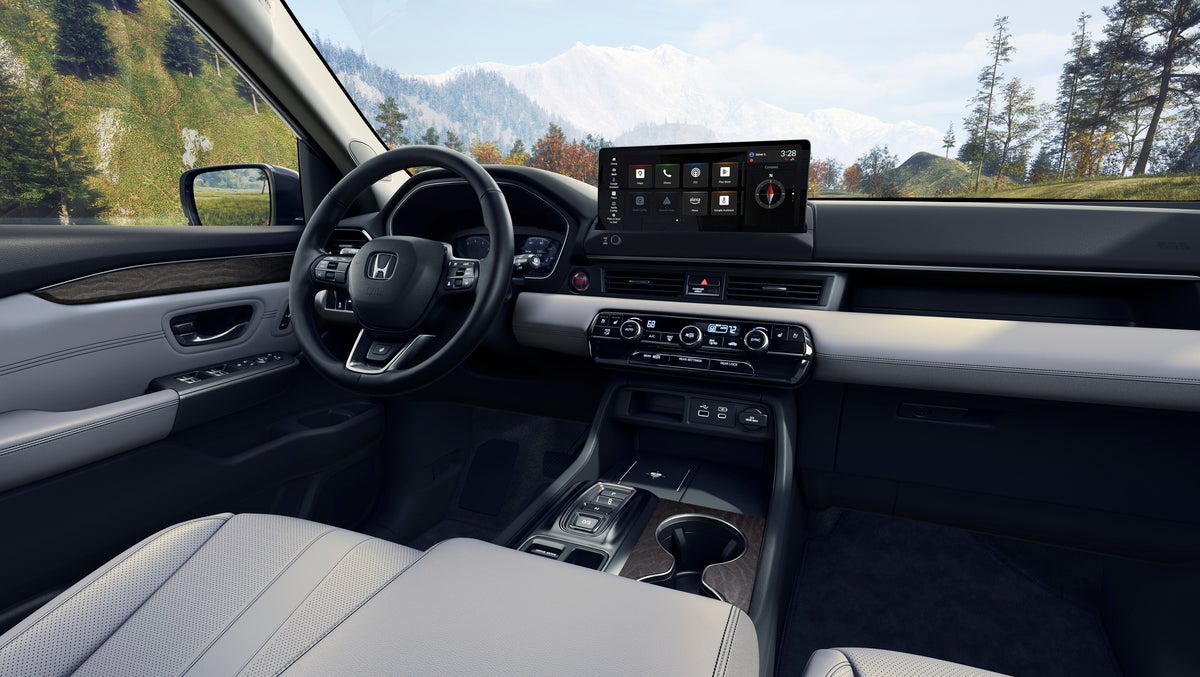 The grey interior of a new Honda Pilot in Phoenix is seen from the back passenger seat looking towards the driver seat.