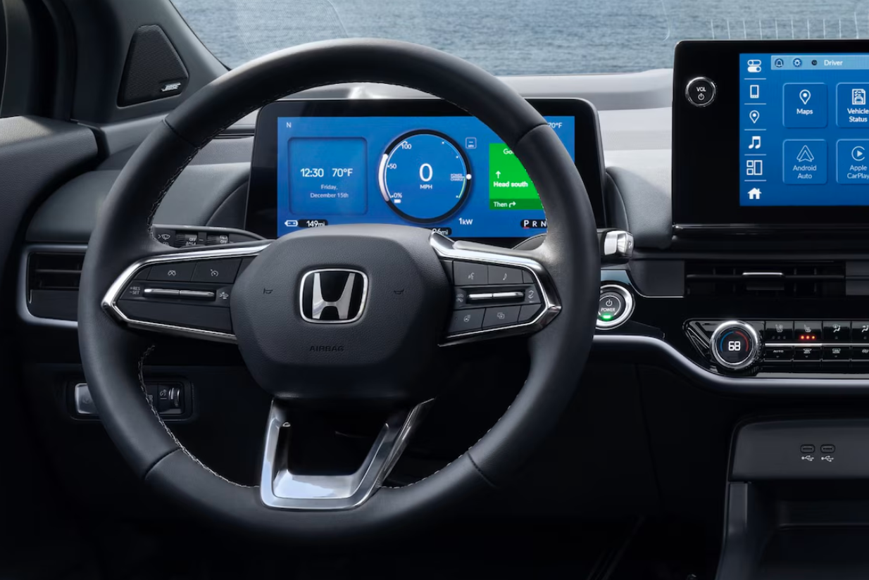 A close-up interior shot of a Honda Prologue, focusing on the steering wheel, digital instrument cluster, and a large vertical infotainment screen. The instrument cluster displays a map and the vehicle's speed, and the infotainment screen shows various app icons.