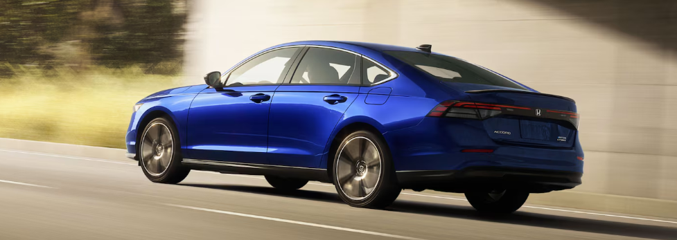 Rear three-quarter view of a blue 2024 Honda Accord Hybrid Touring driving on a road.